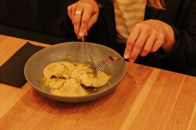 A close up of a woman tucking into a plate of pasta in a dimly lit restaurant.