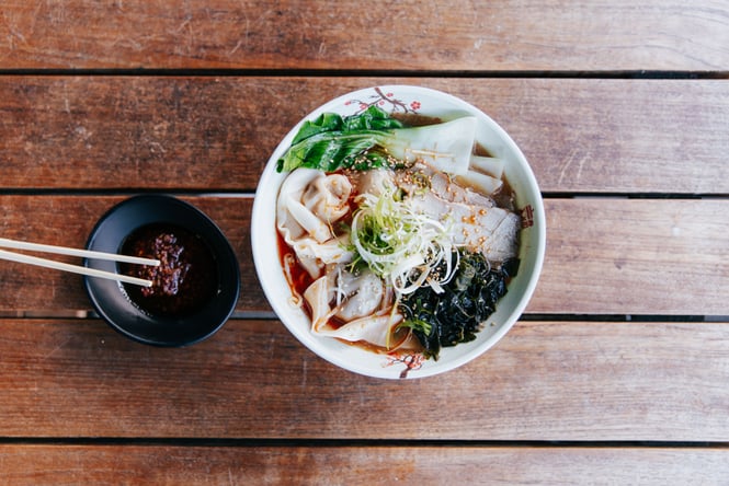 A flatlay of wonton noodle soup and a small bowl of chilli oil.