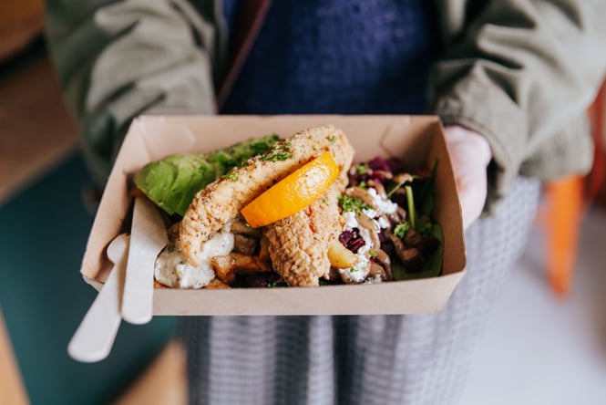 A person holding a cardboard box full of fish and salad.