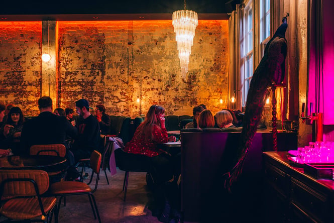 Low lit interior of Puffin Wine Bar with round booths and people sitting underneath a dangling chandelier