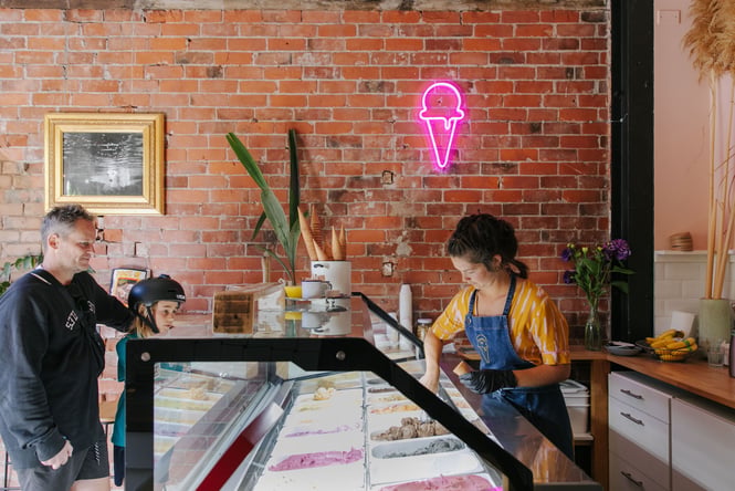 The ice cream cabinet, two customers and one staff member scooping ice cream at Utopia Ice in Christchurch.