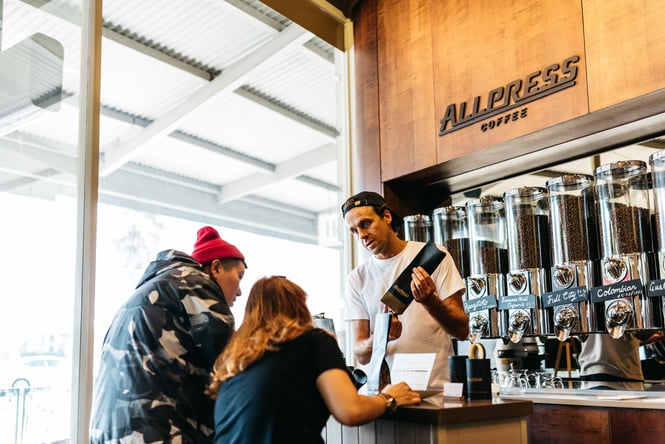 A man holding a bag of Allpress beans talking to two customers.