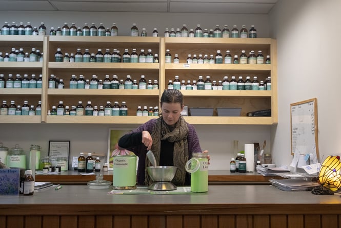 A woman measuring out herbs at a counter.