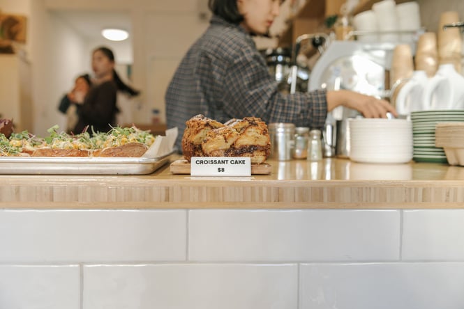 Close up of white tiled cabinet at Noki with a line up of baked goods including croissant cake