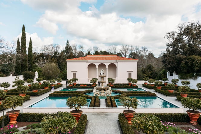 Grand colonial style building with pillars in front of plants and water features at Hamilton Gardens