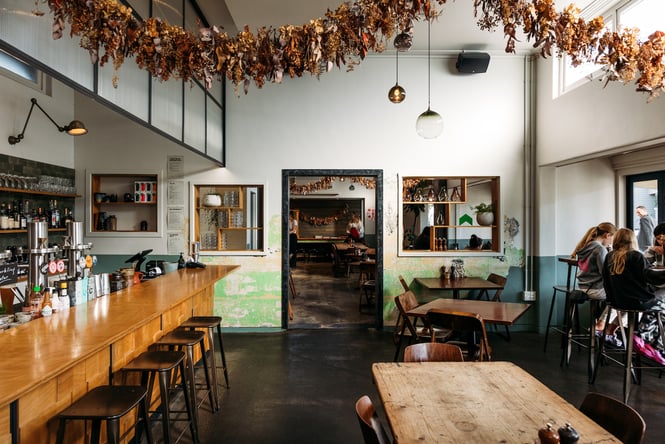 Large modern industrial dining space at Hayes Common in Hamilton with dried flower arrangement hung above