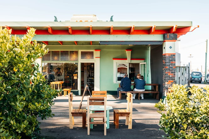 Cute mint green and red exterior of The Lost Boys' cafe in Hamilton with a group of people dining at bench outside