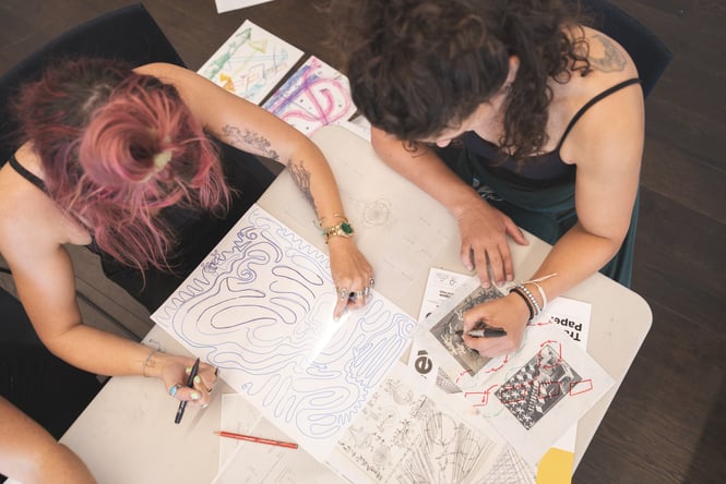 Two visitors to Te Atamira sitting at a table drawing.