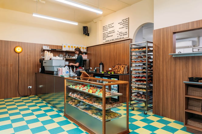 Inside Big Lizard's colourful bakery with green and blue tiled flooring and a fully stocked cabinet of pastries and bread.