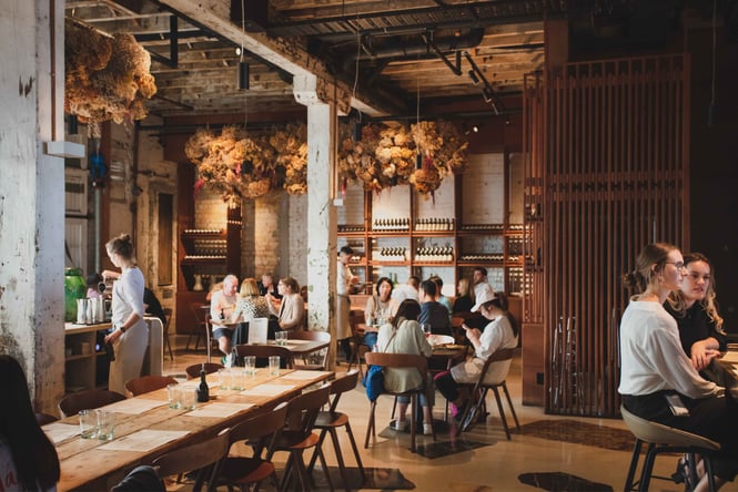 Groups full of people sitting around tables inside a large restaurant space.