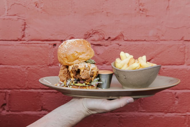 A hand holding a burger and fries on a plate.