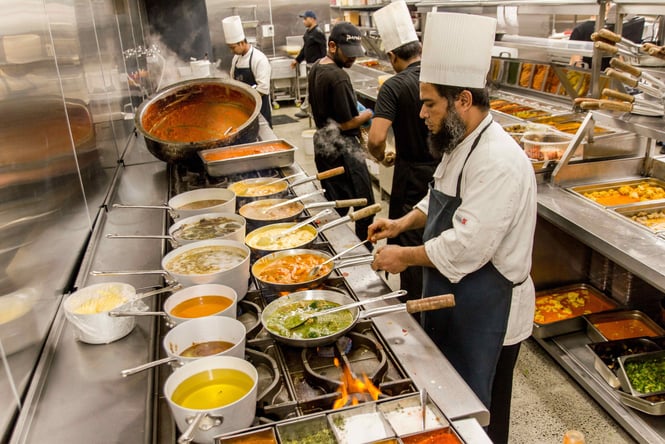 Staff members working in a kitchen cooking curries.