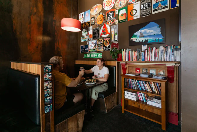 Two people toasting at a booth with beer and plates of food