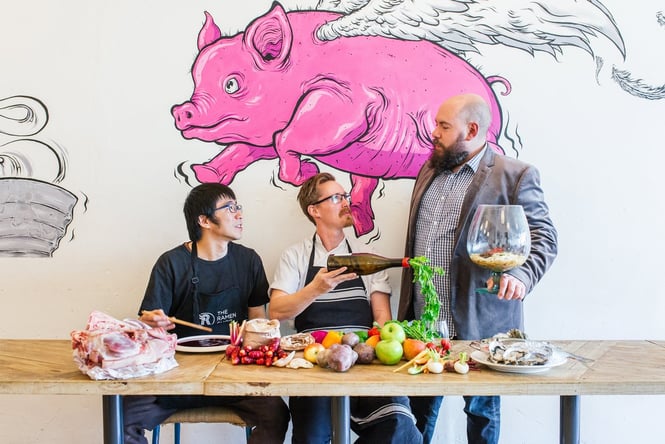A group of men sitting and standing around a table ladened with fresh produce.