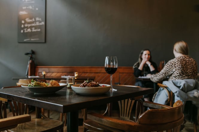 Two plates of a food and a glass of red wine on dark wooden table at Downstairs Bar