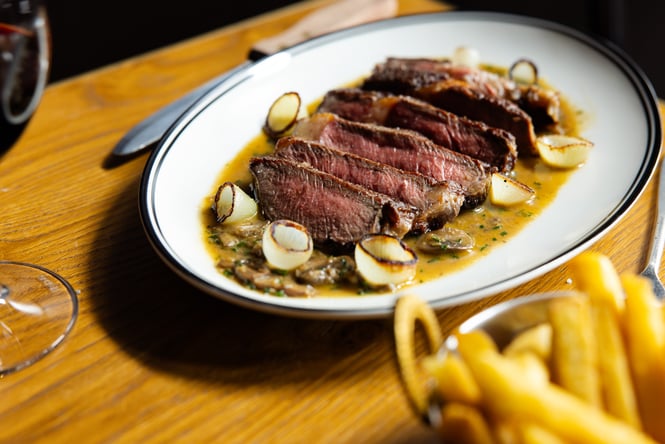 Close up of steak dish with blurred red wine and chips in the foreground