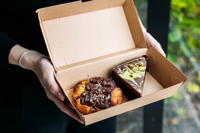 Customer holds a box of treats at Neverland Cakes.