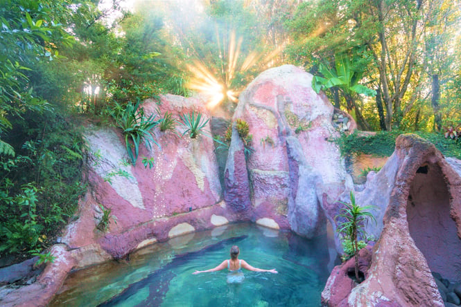 A woman floating in the clear blue water surrounded by big red rocks.