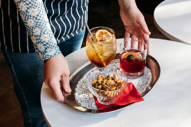 Waiter puts down a cocktail and snack plate on the table.