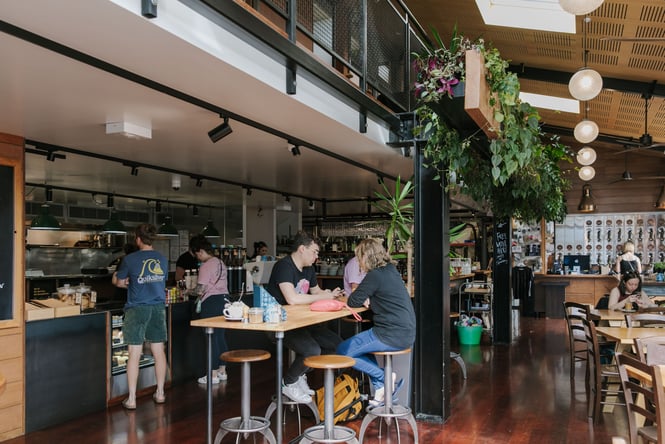 Interior view of cafe with plants, coffee machines and customers sitting at tables drinking coffee
