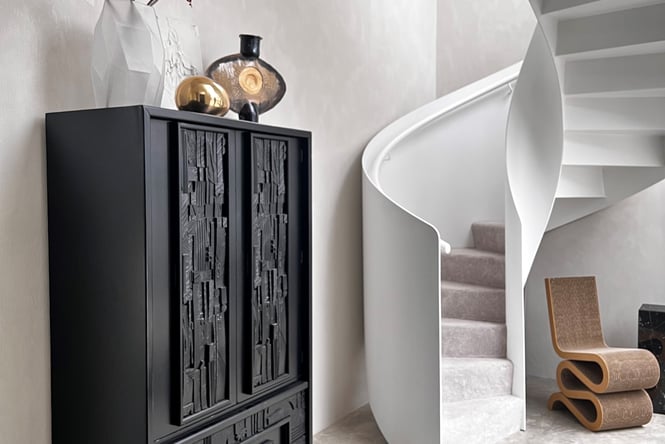 Black mid-century tall cabinet next to a white spiral staircase.