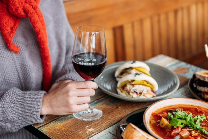 Customer dining at a table with food in front of them and a glass of wine in hand at Pinot Junction.