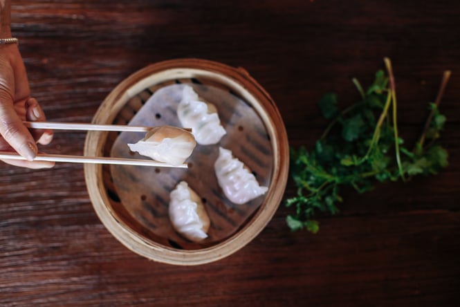 A person using chopsticks to pick up steamed dumplings.