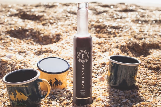 A Barilovska liquer bottle on the beach with assorted mugs.