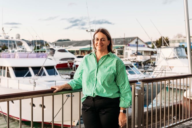 A woman wearing a green shirt smiling to camera in front of boats.