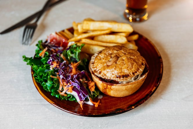 A close up of a pie, salad and chips on a table.
