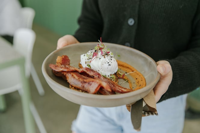 Someone holding a plate of poached eggs with bacon on the side