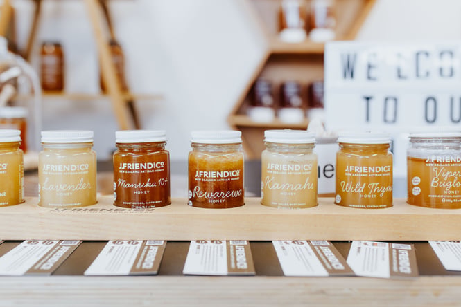 7 jars of honey on a wooden tray.