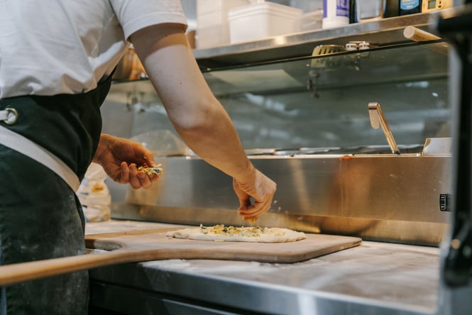A chef making a pizza in a kitchen.