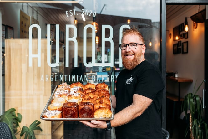 Baker holding a tray of treats from Aurora Argentinian Bakery