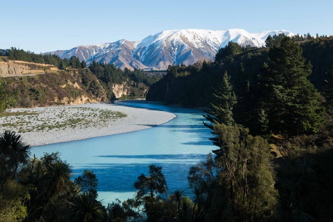 A blue river winding underneath snow covered mountains.