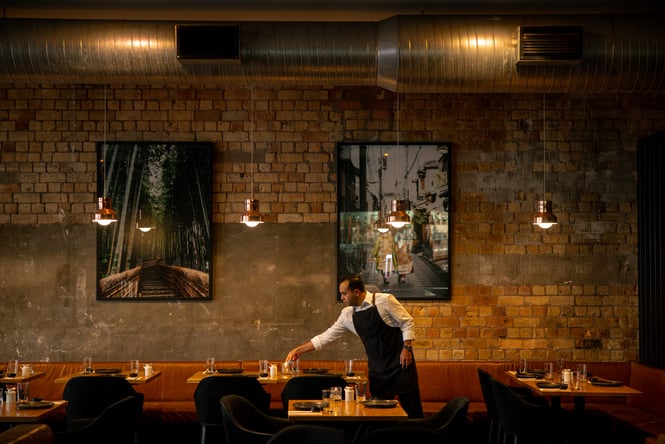 A staff member leaning over a table inside Ebisu restaurant in Auckland.