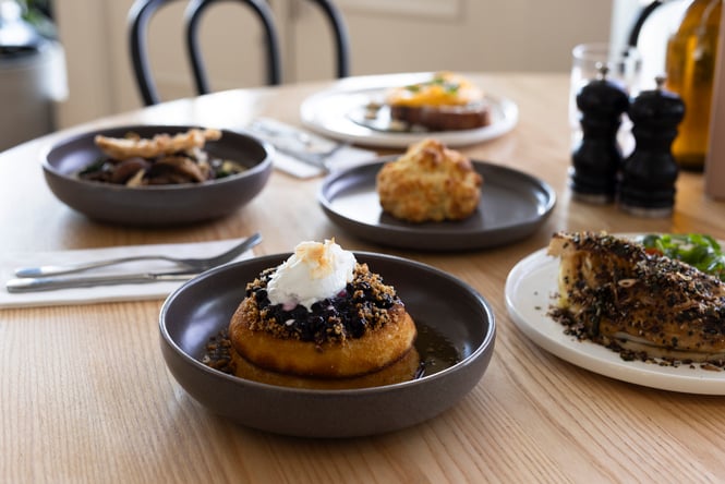 Brunch dishes on cafe table including pancakes with blueberries and a cheese scone