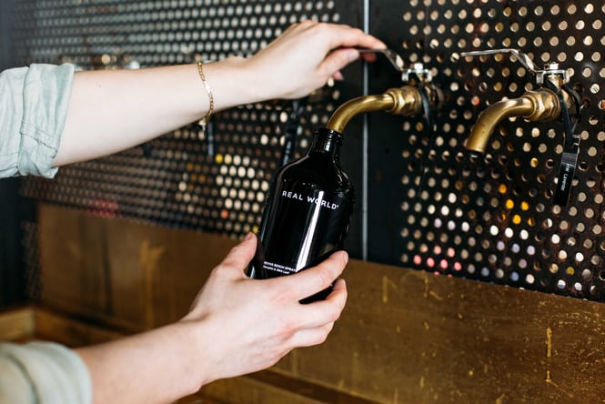 Someone using a zero waste tap to fill up their bottle of Real World skincare in Hastings