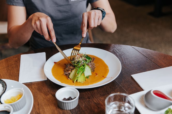 A person with a knife and fork digging into a plate of Filipino food.