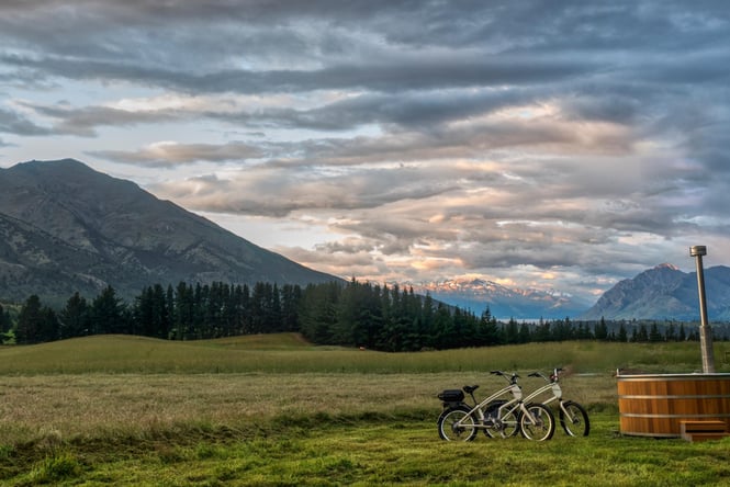 Two bikes standing next to an outdoor hot tub set against a hilly backdrop at sunset.