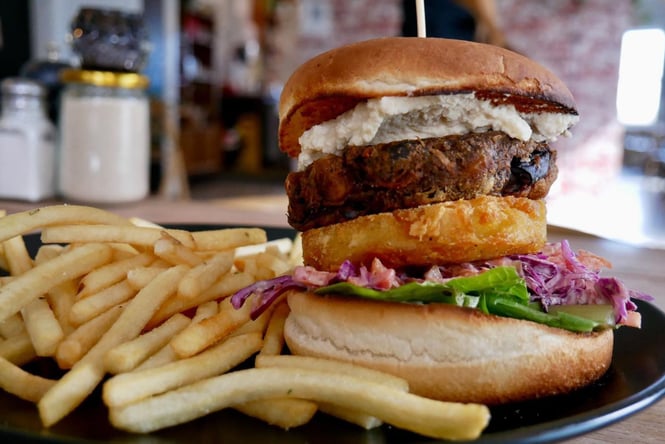 A tall beef burger with a layer of hash browns half together with a long skewer.