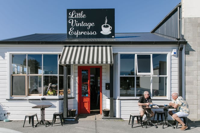 Exterior of Little Vintage Espresso with red door and two men sitting outside in the sun having a coffee