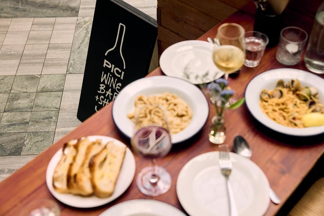 Pici Wine Bar sign with blurred wine glasses and food in front