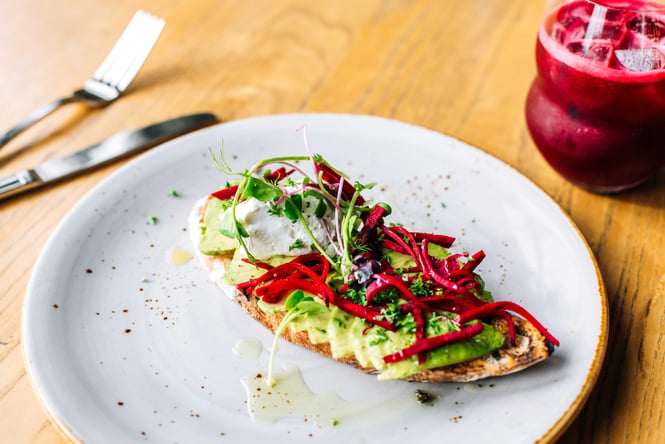 A close up of avocado on toast sitting next to a glass of juice.