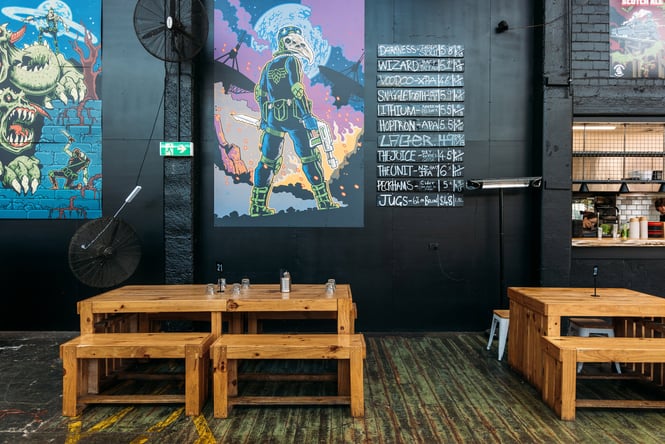Wooden tables and bench seats in front of a black wall decorated with works of art.