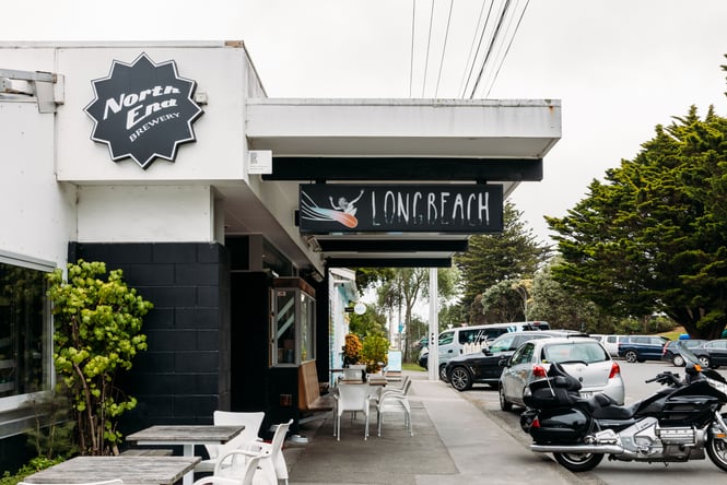 The exterior of Long Beach Tavern with tables and chairs along the footpath.