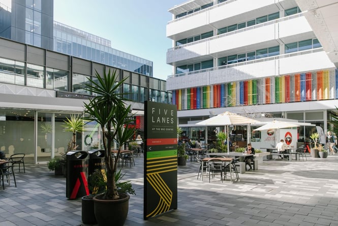 The centre of five lanes where people are sitting at tables under umbrellas.