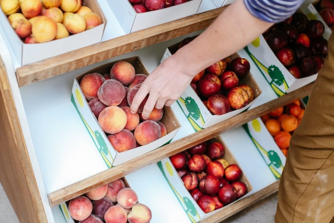 Close up of someone reaching into a box of stone fruit at a roadside stall