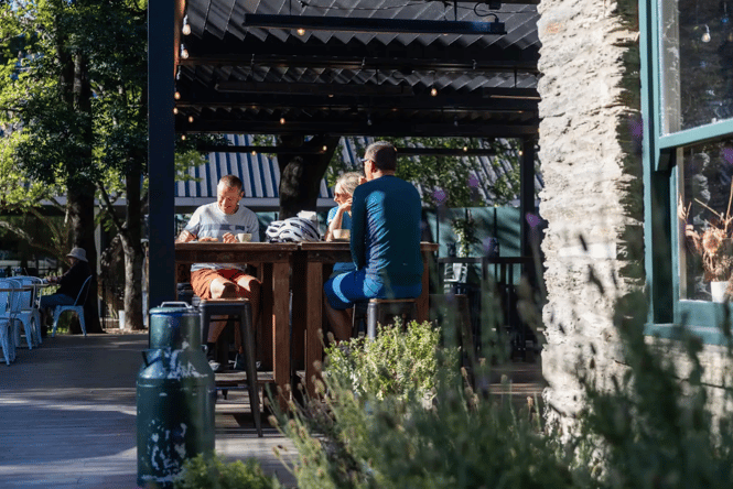 three people sitting together on a high top bar table outside in Queenstown