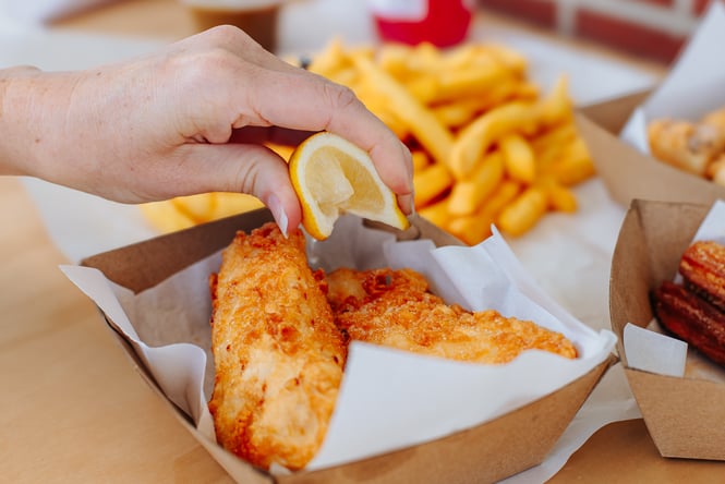 Lemon being squeezed over a portion of fish and chips.